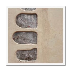 A 20x20 inch framed photo of a stucco beige wall with large irregularly shaped inset stones.