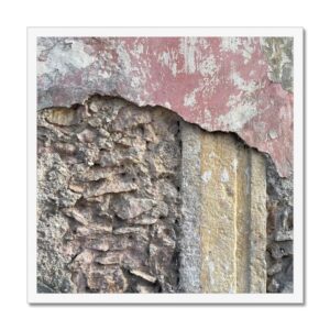 White-framed 20x20 photograph featuring a weathered stone and plaster wall with remnants of pink and yellow paint, revealing layers of history.