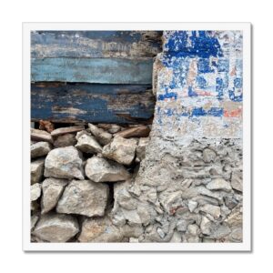 Variety of blue paint shades on wood and worn concrete contrasted by exposed stone framed in 20x20” picture.