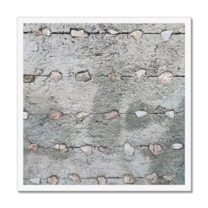 Parallel horizontal rows of small stones embedded in a concrete wall mounted in a white picture frame for hanging.