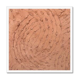 A 20x20” white-framed photo showcasing a textured wall with a design of swirling scratches embedded embedded with small stones.