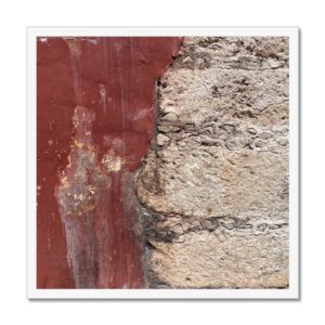 A saucy red wall with stones and concrete on the side, captured in a white 20x20 frame.